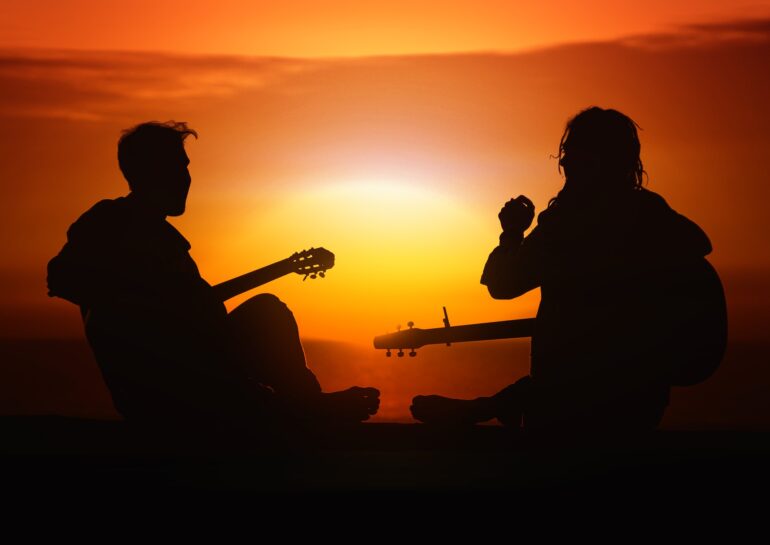 two men sitting together with guitars